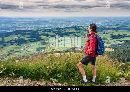 nice senior woman hiking at Mount Gruenten in the Allgaeu Alps with awesomw view over Iller valley to Lake Alpsee and Lake of Constanz, Bodensee,  Bav Stock Photo