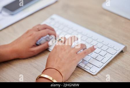 Closeup of one business womans hands and fingers typing on desktop computer keyboard at a table in an office. One female only sending emails while Stock Photo
