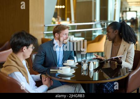 Young African American businesswoman making presentation of new project to intercultural male colleagues during meeting in cafe Stock Photo