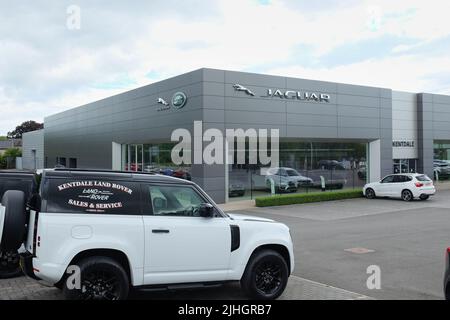 Kentdale Jaguar Land Rover garage with A Land Rover Defender in the foreground and the large, modern dealership building behind with the Jaguar brand Stock Photo