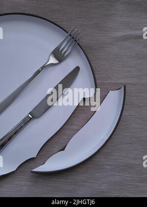 Tableware lay over the broken plate. Knife and fork on the dining plate. Misfortune in the kitchen. Stock Photo
