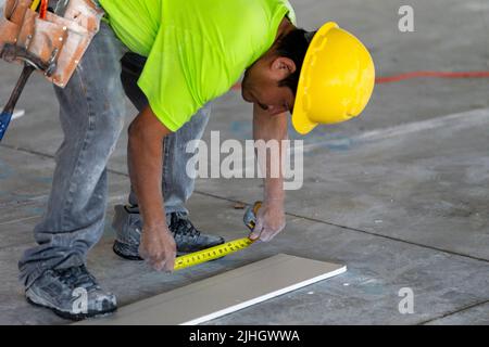 Qualified construction worker is measuring a piece of drywall for cutting, sanding and installation onto metal framing in a residential apartment Stock Photo