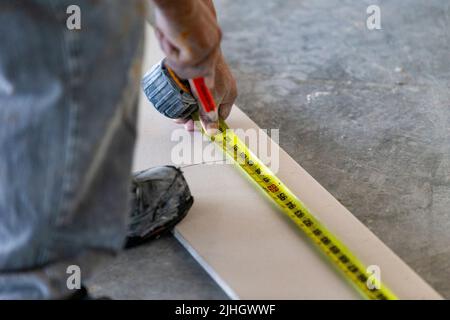 Qualified construction worker is measuring a piece of drywall for cutting, sanding and installation onto metal framing in a residential apartment Stock Photo