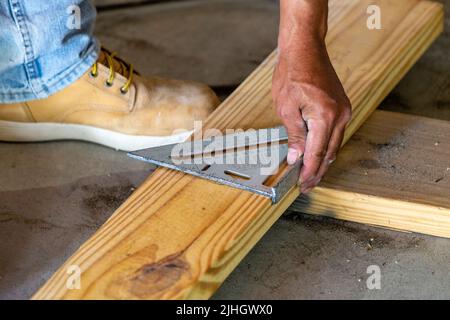 Construction worker using a carpenters square to measure and mark a wooden beam for cutting. 2x6. The wood is a support beam between steel struts. Stock Photo