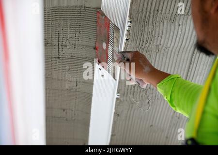 Construction worker using a notched trowel to rake the stucco mud for further stucco mud application for weather sealing the exterior of the building Stock Photo