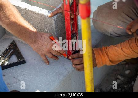 construction workers marking lines on a concrete slab, measured by a level and installed masonry string with a pencil. Stock Photo