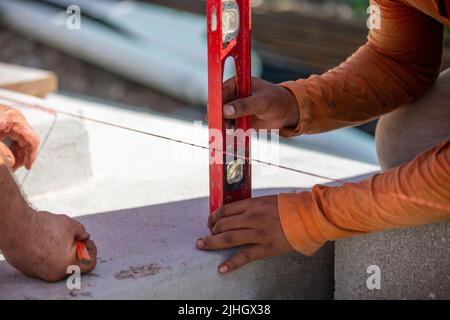 Two construction workers, masons, using a level to mark and measure from a red line spanned before Stock Photo