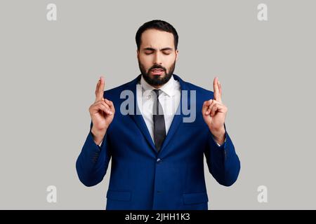 Hopeful handsome bearded man showing time out gesture, looking with imploring eyes, hurry to meet deadline, wearing official style suit. Indoor studio shot isolated on gray background. Stock Photo