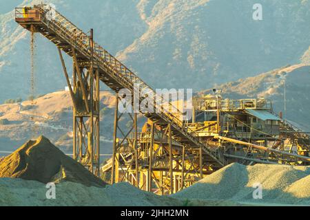 Belt conveyor transports crushed stone from grinder to stockpile at sunset. Stock Photo