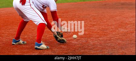 A high school baseball player fielding the ball on red turf field during a game. Stock Photo