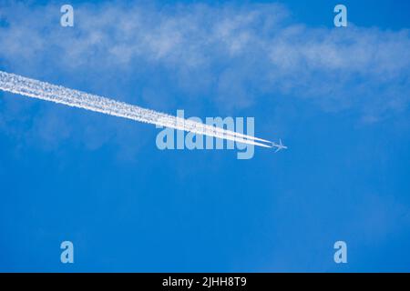 White aircraft vapour trails from a jet against a blue sky on a sunny day in summer in Surrey, south-east England from a Heathrow Airport flight Stock Photo