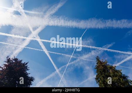 White aircraft vapour trails and clouds against a blue sky on a sunny day in summer in Surrey, south-east England from Heathrow Airport flights Stock Photo