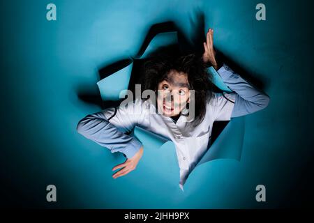 Lunatic silly chemist with messy hairstyle, looking funny while making humorous gestures at camera. Foolish insane scientist with wacky look and dirty face after laboratory explosion acting crazy. Stock Photo