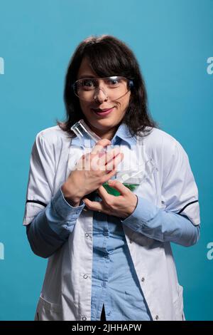 Wild looking laboratory worker holding beakers filled with unknown liquid substances while on blue background. Mad crazy looking chemistry expert having Erlenmeyer glass flasks while acting insanely. Stock Photo