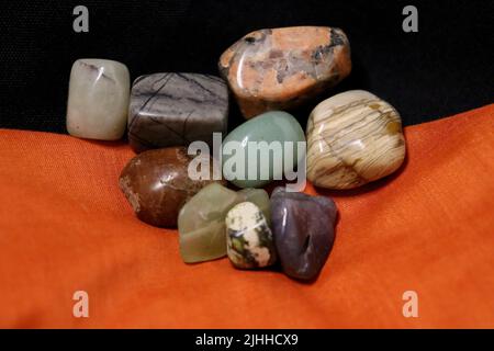 A group of polished gemstones on top of black and orange fabric napkins with an auger shell. Stock Photo