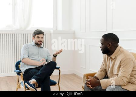 A male psychologist conducts psychological therapy with an African American man, makes notes in a clipboard Stock Photo