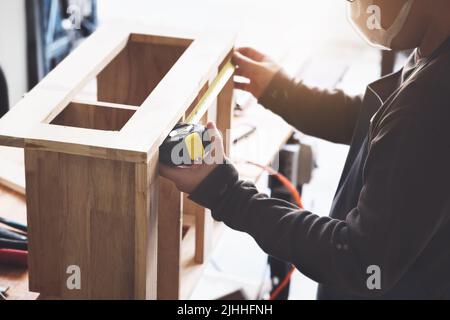 A carpenter measures the planks to assemble the parts and build a wooden table for the customer Stock Photo