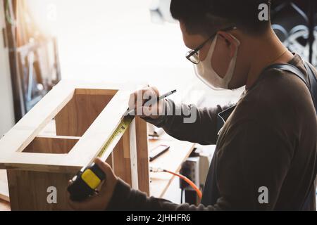 A carpenter measures the planks to assemble the parts, and build a wooden table for the customer Stock Photo