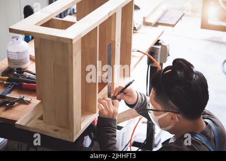 A carpenter measures the planks to assemble the parts, and build a wooden table for the customer Stock Photo