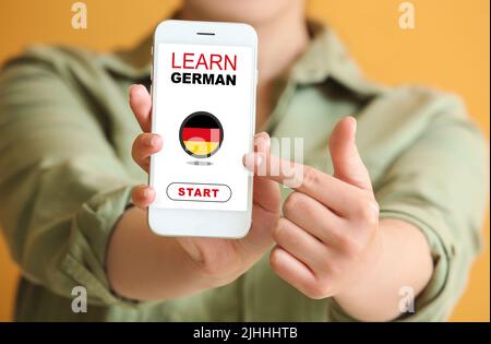 Woman holding mobile phone with text LEARN GERMAN on screen, closeup Stock Photo