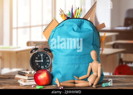 School backpack with stationery, wooden human figurine, clock and apple on table in classroom Stock Photo
