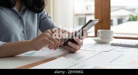 Close up hand of business woman or accountant using mobile phone and working for financaial chart graph report. Stock Photo