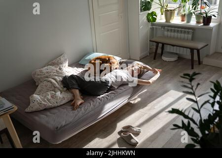 Woman lying in bed with dog in morning, relaxing after waking up, stretching body after sleeping Stock Photo