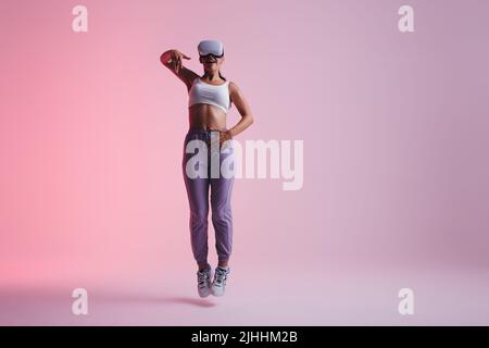 Energetic young woman dancing in the metaverse. Active young woman enjoying herself while wearing virtual reality goggles. Woman having fun while expl Stock Photo