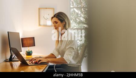 Young businesswoman typing on a laptop while sitting in her home office. Female entrepreneur writing an email to her business clients while working fr Stock Photo