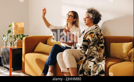 Interior designers discussing a new idea while sitting in the lobby of a modern office. Two businesswomen using a digital tablet while working togethe Stock Photo