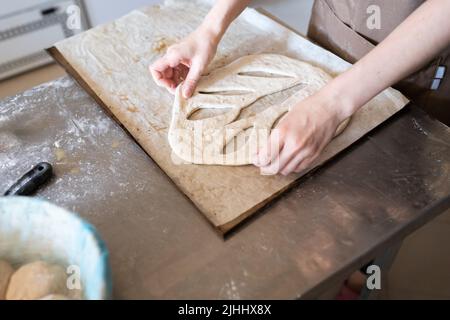A baker shapes and cuts traditional French Fougasse bread. Front view. Stock Photo