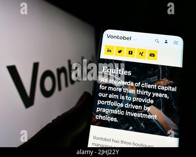 Person holding cellphone with webpage of Swiss financial company Vontobel Holding AG on screen with logo. Focus on center of phone display. Stock Photo