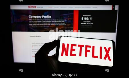 Person holding smartphone with logo of US video streaming company Netflix Inc. on screen in front of website. Focus on phone display. Stock Photo