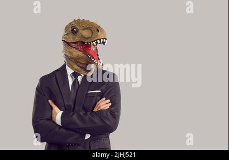 Funny man with dinosaur mask on head stands in studio with arms crossed dressed in business suit Stock Photo