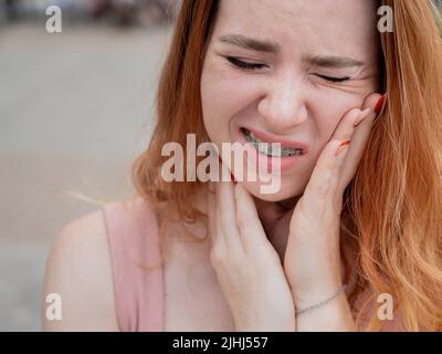 Young red-haired woman with braces suffering from pain.  Stock Photo