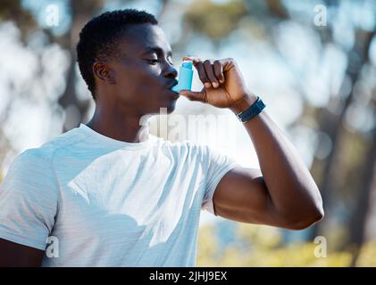 Young african man taking a break from a workout to use his asthma pump. Fit athlete using his asthma inhaler during an asthma attack while exercising Stock Photo