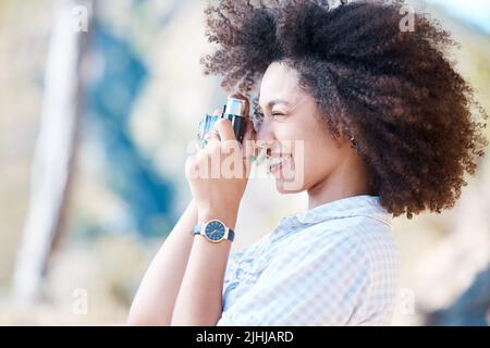 One young smiling mixed race woman with afro holding and using a camera to take photographs. Happy hispanic woman with curly hair taking pictures Stock Photo