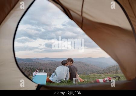 View from inside tent on beautiful landscape of mountains and couple kissing. Love and travel.  Stock Photo