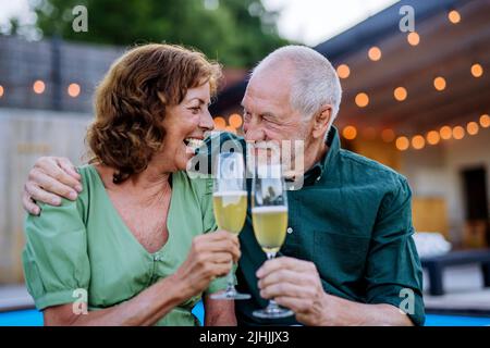 Senior man with number with his wife celebrating birthday and toasting with wine near backyard pool. Stock Photo