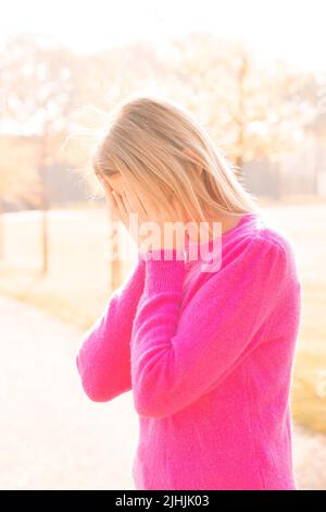 Tired, sad or depressed young beautiful blonde woman burries her face in her hands being frightened, having anxiety attack or headache migraine or depression, upset frustrated girl troubled with problem feel stressed cover crying face with hand suffer from grief sorrow concept. High quality photo Stock Photo