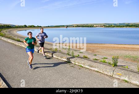 Lewes UK 19th July 2022 - Early morning runners at Arlington Reservoir near Lewes in East Sussex on another hot sunny day with temperatures forecast to exceed 40 degrees in some parts as an extreme red weather warning has been issued for today throughout parts of Britain : Credit Simon Dack / Alamy Live News Stock Photo