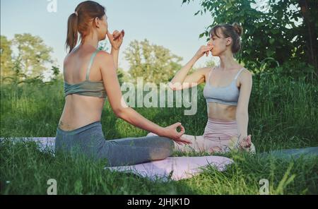 Two young women doing breathing practice and doing yoga outdoor Stock Photo