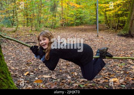 Sheffield, UK - 31 Oct 2019: a girl laughs as she balances on a thin tree branch in Autumns woodland at Eccleshall Woods Stock Photo