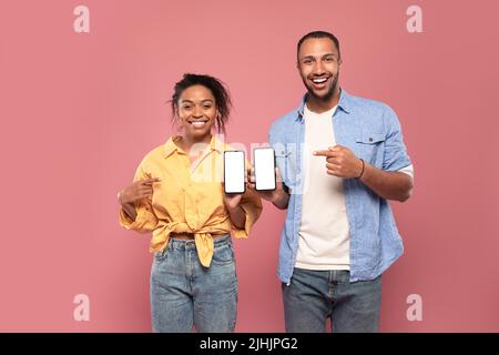Use this new application. Happy black couple holding 2 smartphones in hands and pointing at empty screen, mock up Stock Photo