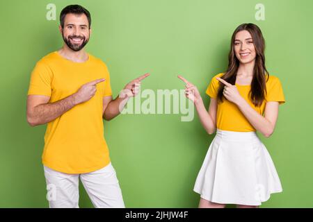 Portrait of two positive people indicate fingers empty space each other isolated on green color background Stock Photo