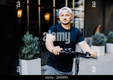 Pleasant smiling man riding a kick scooter. Happy man riding kick scooter Stock Photo