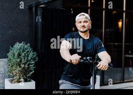 Pleasant smiling man riding a kick scooter. Happy man riding kick scooter Stock Photo