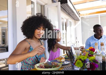 Multiracial mother and father having lunch with daughter while sitting at dining table at home Stock Photo