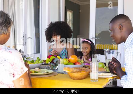 Multiracial multigeneration family praying before having lunch while sitting at dining table at home Stock Photo