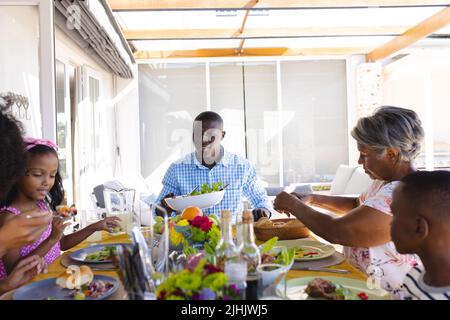 Multiracial multigeneration family eating lunch while sitting at dining table at home Stock Photo